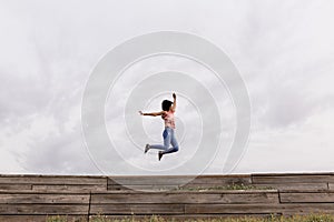 Happy young beautiful afro american woman listening to music in her mobile phone and jumping. Cloudy background. Spring or summer