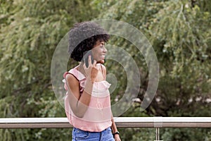 Happy young beautiful afro american woman smiling and using mobile phone. Green background. Spring or summer season. Casual