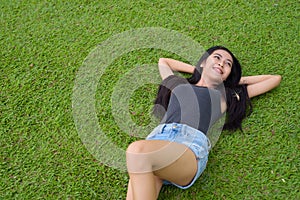 Happy young beautiful Asian woman laying down on grass at the park