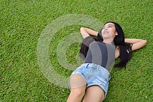 Happy young beautiful Asian woman laying down on grass at the park