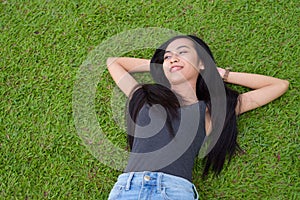 Happy young beautiful Asian woman laying down on grass at the park