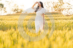 Happy young beautiful Asian woman in white dress standing in the barley field enjoying her time outdoor alone during sunset