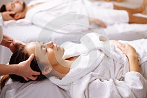 Happy young beautiful couple enjoying head massage at the spa