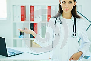 Happy young beautiful female doctor showing blank area for sign or copyspace.