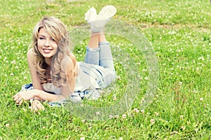 Happy young beautiful girl lying on the grass and smiles in jeans in a Sunny summer day in the garden