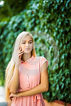 Happy young beautiful woman calling by phone in autumn on wall leaves green