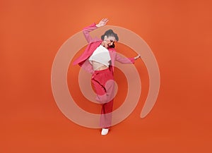Happy young beautiful woman dancing isolated on orange background in studio. People lifestyle concept