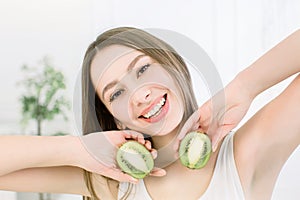 Happy young beautiful woman holding slices of kiwi fruit near her face - isolated on light background