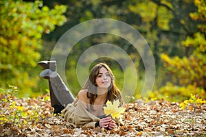 Happy young beautiful woman laying on autumn leaves.
