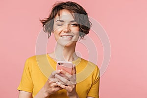 Happy young beautiful woman posing isolated over pink wall background using mobile phone