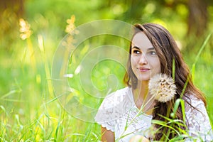 Happy young beautiful woman sitting on grass with dandelion flow