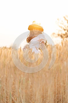 Happy young beautiful woman wearing black hat and white dress enjoying herself walking in the golden barley filed on a late