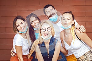 Happy young best friends taking funny selfie with open face masks after lockdown reopening