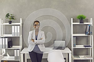 Happy young black businesswoman in suit and glasses standing in modern office interior