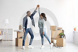 Happy Young Black Couple Celebrating Moving To New Flat, Dancing Among Boxes