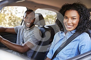 Happy young black couple driving in a car smiling to camera