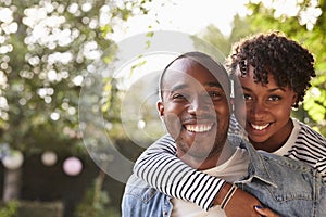 Happy young black couple piggyback in garden, look to camera