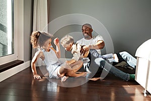 Happy Young Black Family Playing Together On Floor At Home In Living Room. Funny dad having fun with two kids. African