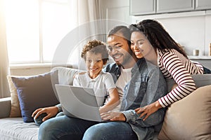 Happy young black family of three using laptop together at home