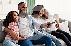 Happy young black family watching television sitting on sofa