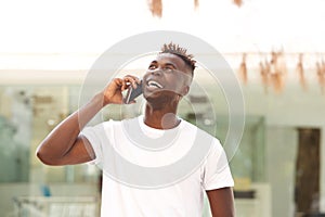 Happy young black guy standing outdoors and making a phone call