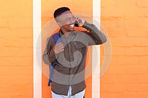 Happy young black guy talking on mobile pone by orange wall