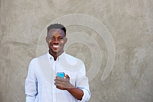 Happy young black man with mobile phone standing by wall