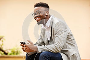 Happy young black man sitting outside listening to music with earphones