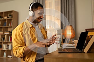 Happy young black man using laptop, wearing headphones, having video chat at home, copy space