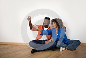 Happy Young Black Spouses Sitting On Floor And Holding Home Keys