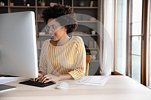 Happy young Black student girl in glasses working at desktop