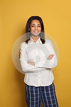 Happy young black woman with crossed arms standing against bright yellow background