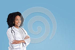 Happy young black woman doctor therapist in white coat with crossed arms on chest looks at free space