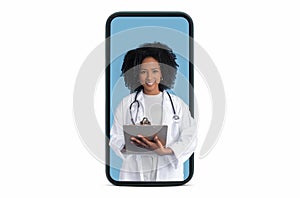 Happy young black woman doctor therapist in white coat making notes on big smartphone screen