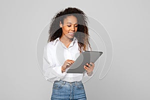 Happy young black woman engaging with digital tablet, gray background