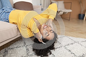 Happy young black woman in headphones lying on couch with closed eyes, listening to music at home, copy space