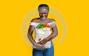 Happy Young Black Woman Holding Eco Bag With Groceries On Yellow Background