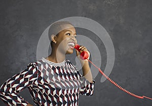 Happy young black woman holding the receiver of her landline telephone and talking