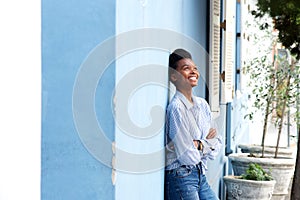 Happy young black woman leaning against wall