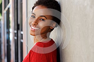 Happy young black woman leaning against wall and smiling