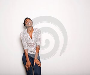 Happy young black woman leaning on white wall laughing