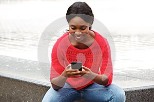Happy young black woman looking cellphone in the city