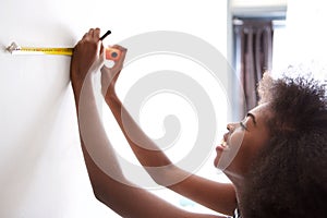 Happy young black woman measuring on wall