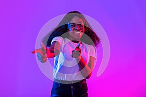 Happy young black woman pointing fingers at camera, choosing you, smiling in neon light