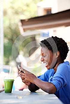 Happy young black woman sitting at cafe reading text message on cell phone