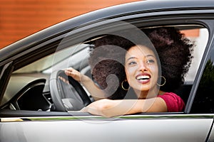 Happy young black woman sitting in driver seat of car in daylight