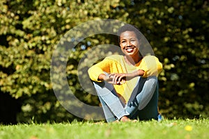 Happy young black woman sitting on grass outdoor