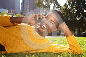 Happy young black woman smiling outdoors in park and talking with mobile phone