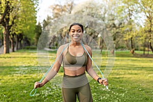 Happy young black woman in sportswear posing with jumping rope at city park