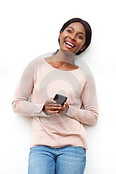 Happy young black woman standing against white wall with cellphone in hand